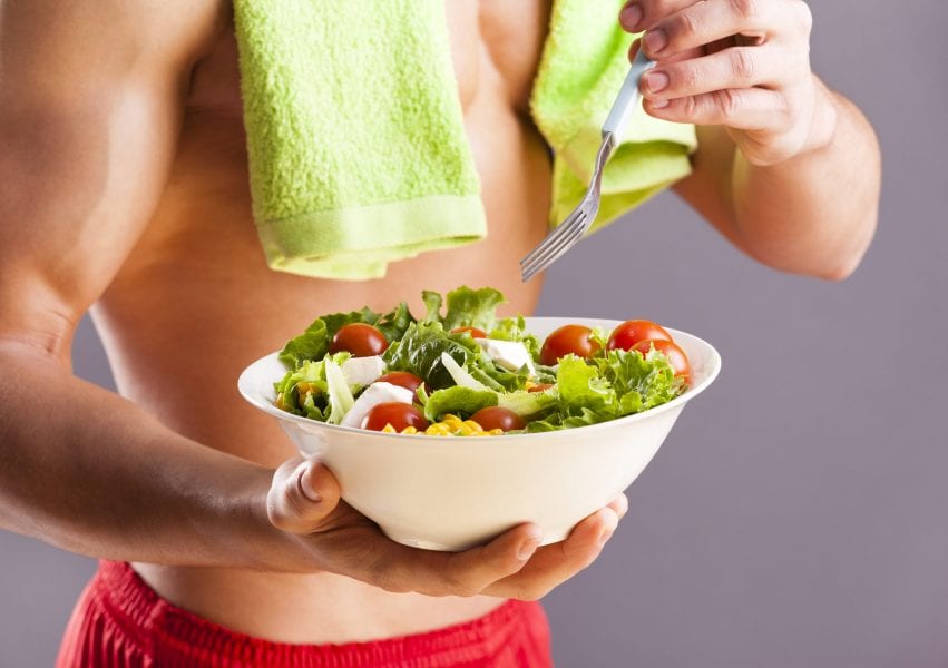 Fit man holding a bowl of fresh salad on grey background